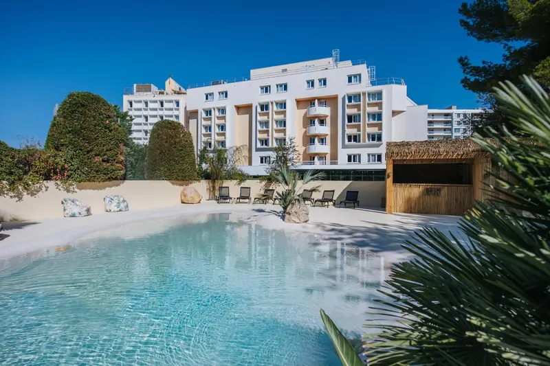 Vue d'une piscine devant un bâtiment blanc avec des transats.