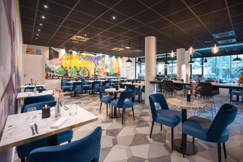 Une salle de restaurant lumineuse avec des tables dressées et des chaises bleues.