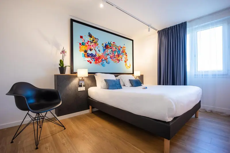 Une chambre lumineuse avec un grand lit et une décoration murale colorée.