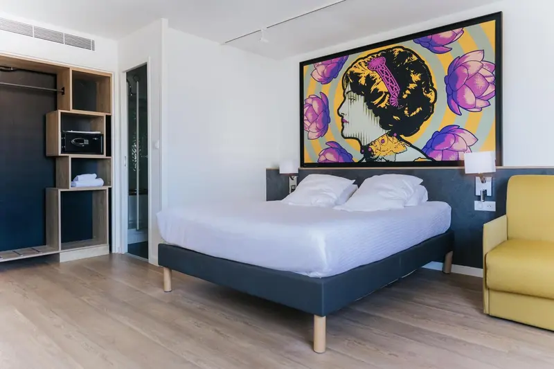 Une chambre lumineuse avec un grand lit et une décoration murale colorée.