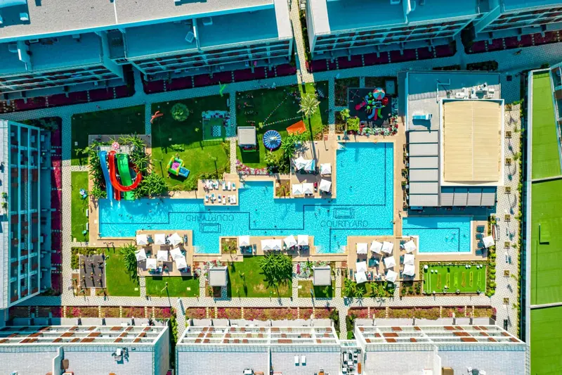 Vue aérienne d'une piscine avec transats et jeux d'eau dans un complexe hôtelier.