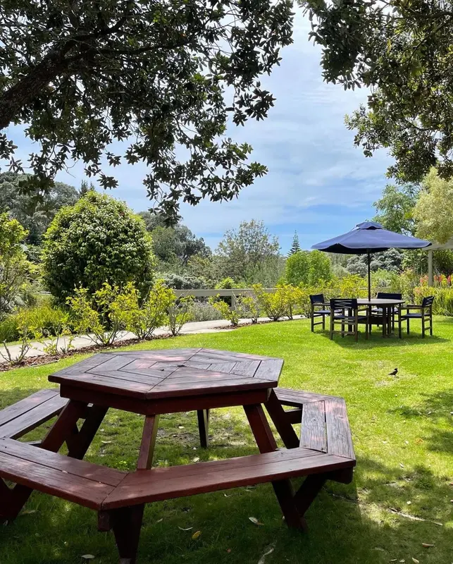 Une table en bois est entourée de bancs dans un jardin verdoyant.