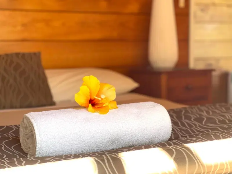 Un lit soigneusement fait avec une fleur jaune posée sur une serviette.
