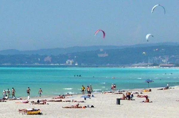 Une plage de sable fin bordée d'une eau turquoise, avec des personnes se relaxant et pratiquant des sports nautiques.