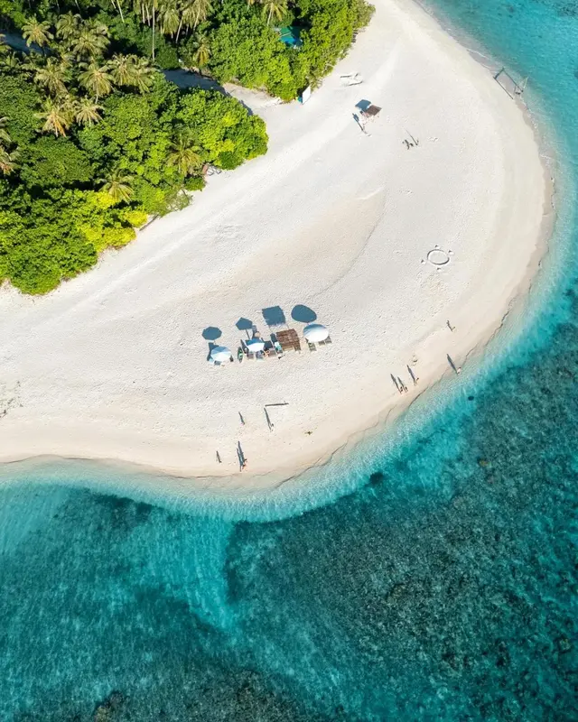 Vue aérienne d'une plage de sable blanc bordée d'eau turquoise et de végétation luxuriante.