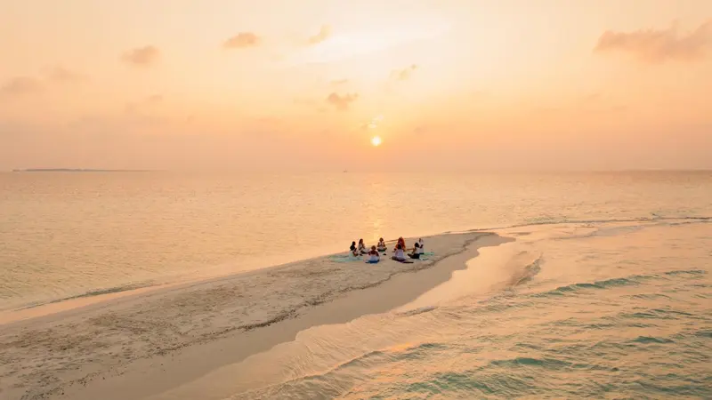 Un groupe de personnes se détend sur une plage de sable blanc au coucher du soleil.