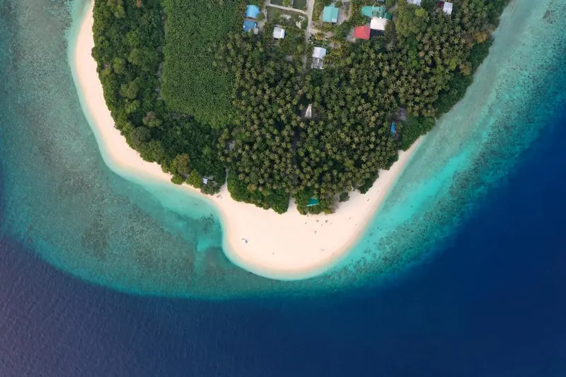 Vue aérienne d'une île tropicale bordée d'une plage de sable blanc et d'une végétation luxuriante.