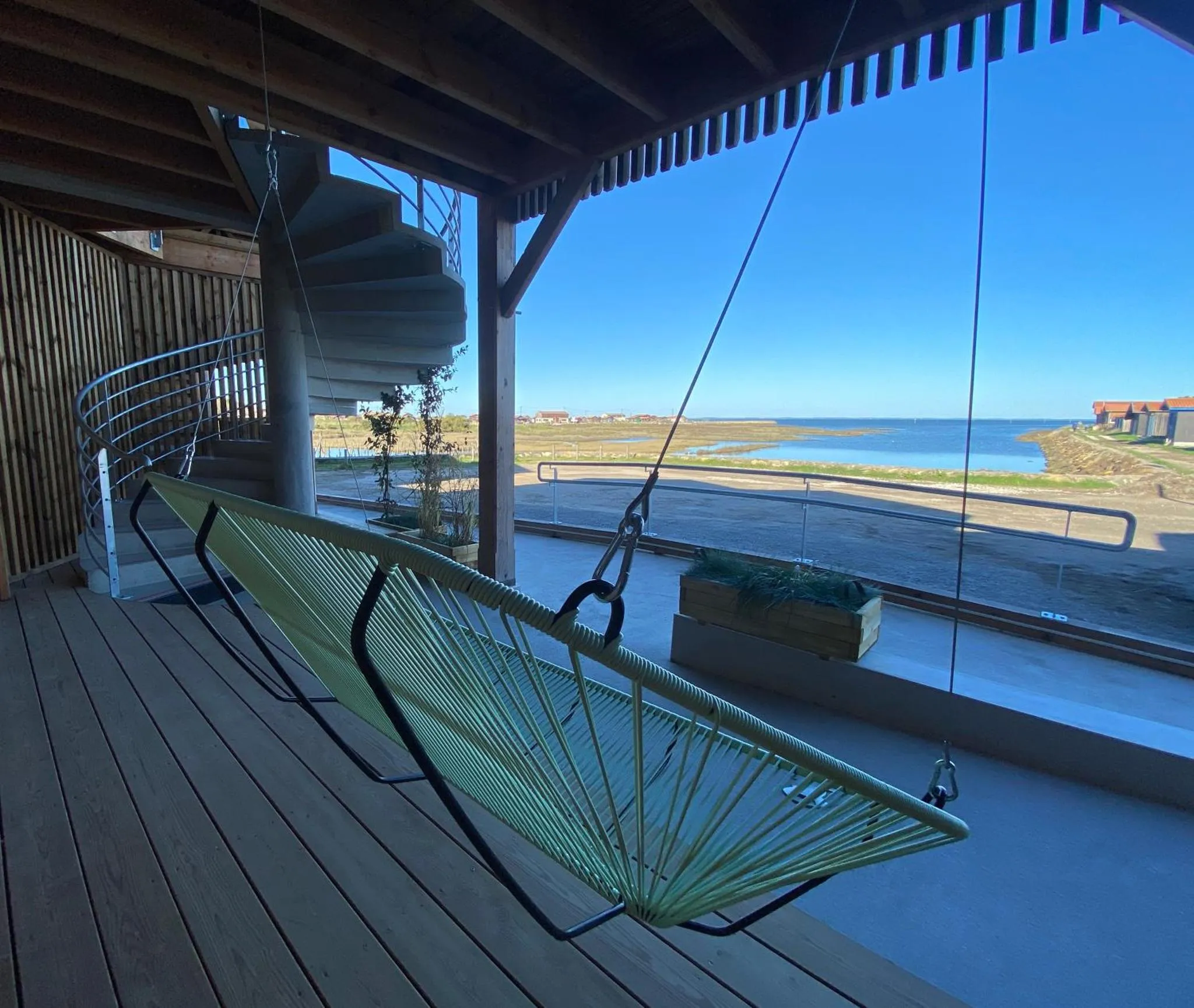 Un hamac est suspendu sur une terrasse en bois avec vue sur la mer.