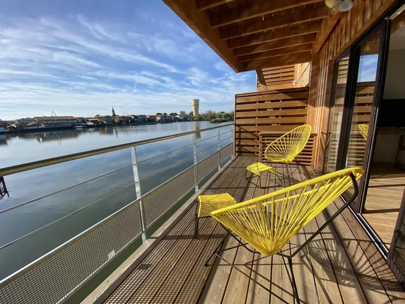 Terrasse en bois avec deux fauteuils jaunes donnant sur une rivière et une ville en arrière-plan.