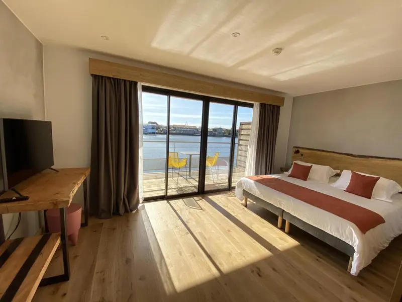 Chambre lumineuse avec un grand lit et une vue sur une terrasse ensoleillée.