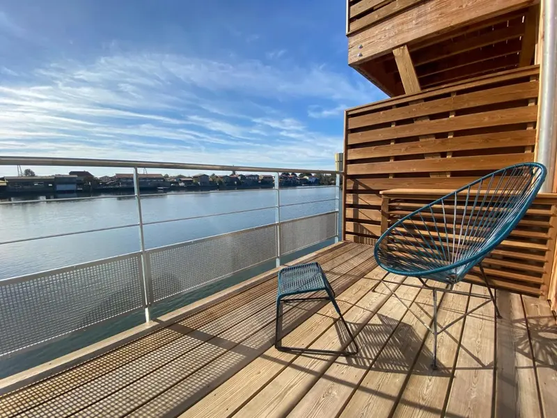 Terrasse en bois avec mobilier d'extérieur donnant sur une étendue d'eau et un ciel nuageux.