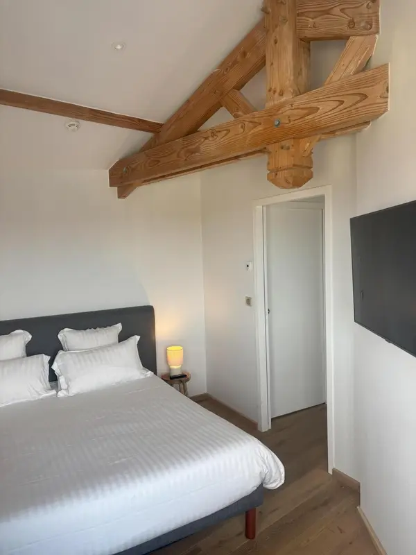 Une chambre lumineuse avec un lit double et une structure en bois au plafond.