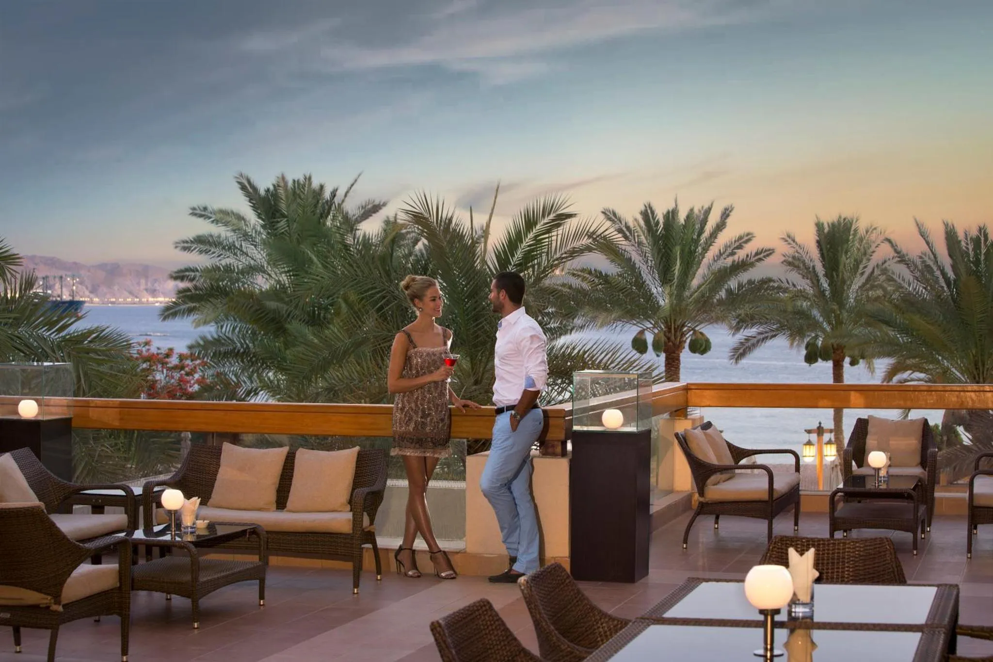 Un couple discute sur une terrasse avec vue sur la mer et les palmiers.