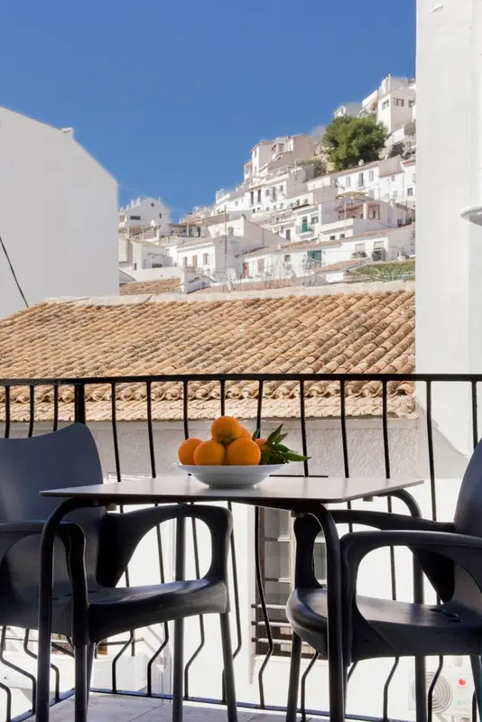 Une table et des chaises noires sont disposées sur une terrasse avec vue sur un village blanc.