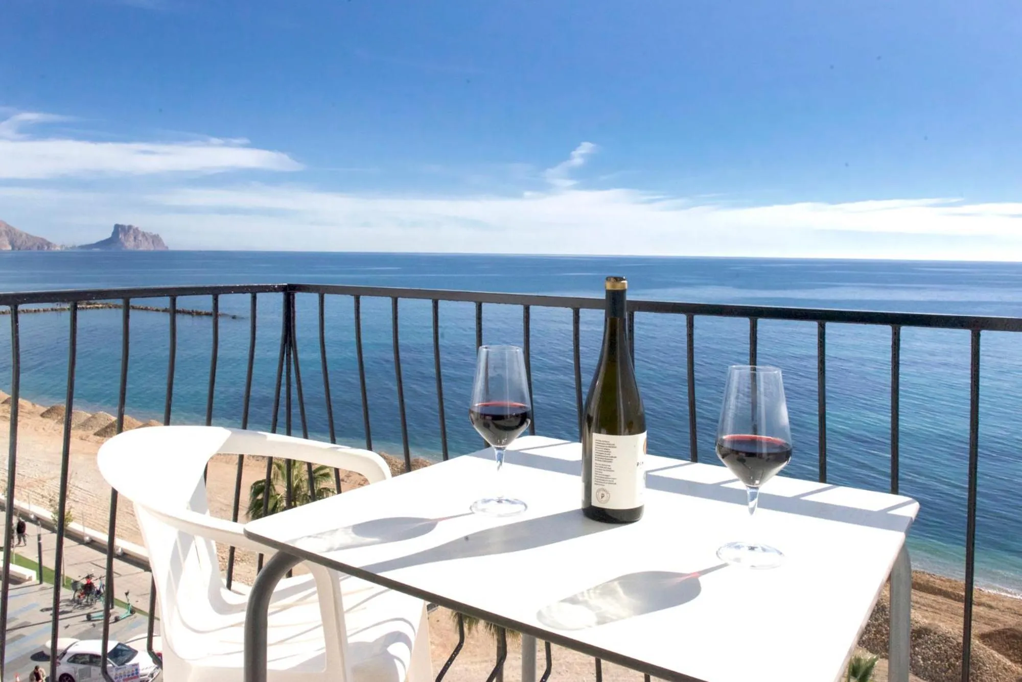 Une table avec des verres de vin et une bouteille sur un balcon avec vue sur la mer.