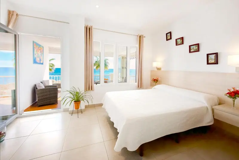 Chambre lumineuse avec un grand lit blanc et une vue sur la mer.