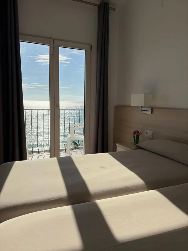 Une chambre lumineuse avec un lit et une vue sur la mer depuis un balcon.