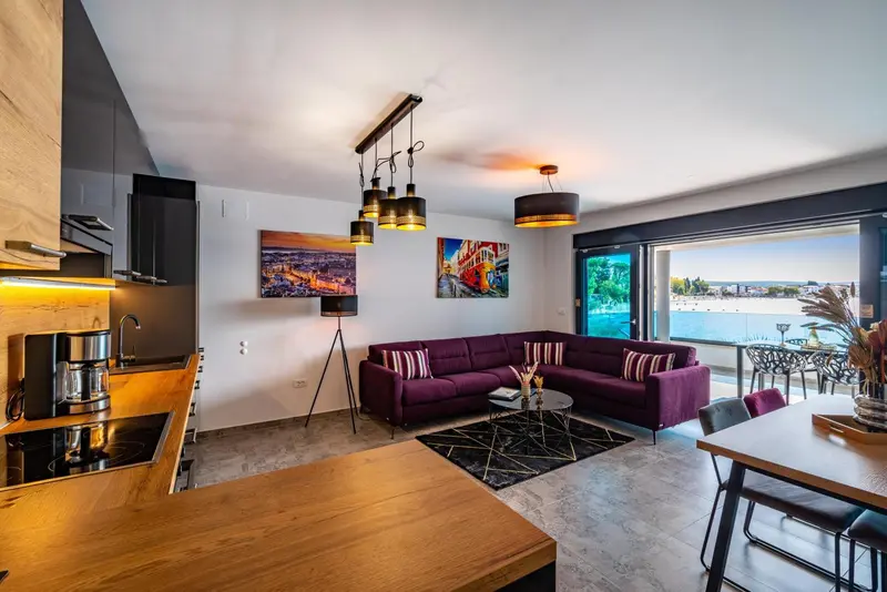 Un espace de vie moderne avec un canapé violet et une cuisine ouverte donnant sur une terrasse.