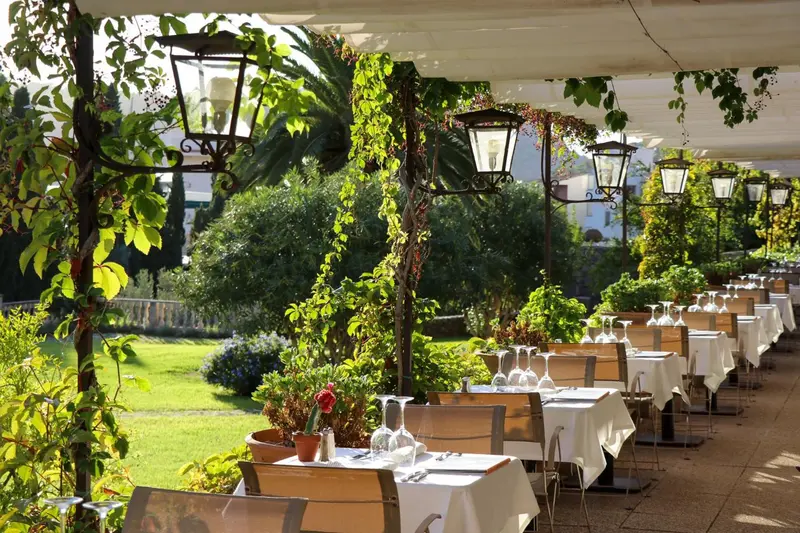 Terrasse ombragée avec tables dressées et végétation luxuriante.