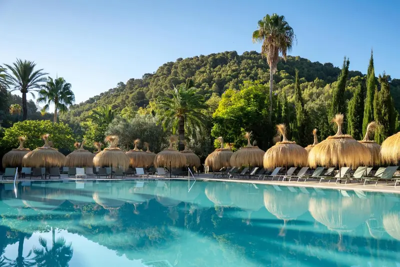 Transats alignés au bord d'une piscine turquoise sous des parasols de chaume.