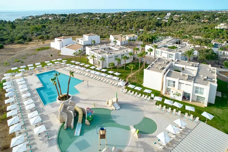 Vue aérienne d'un complexe hôtelier blanc avec piscine et toboggan aquatique.