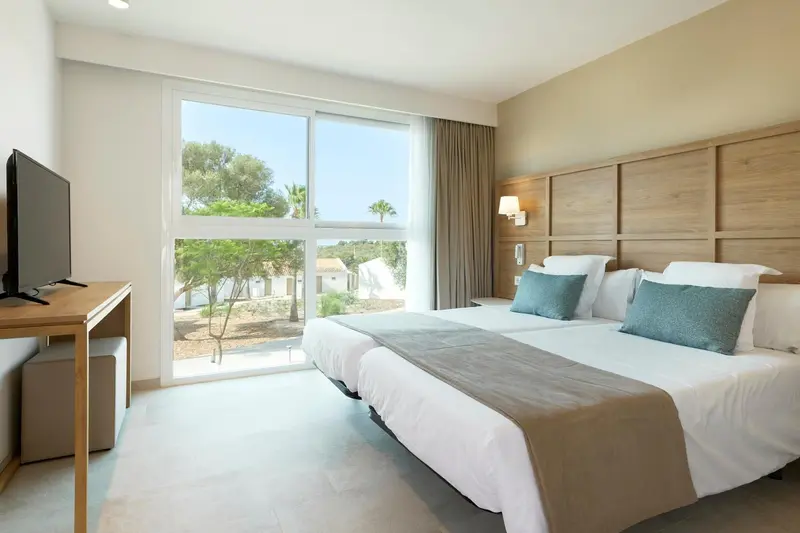 Chambre lumineuse avec deux lits simples et vue sur la végétation.