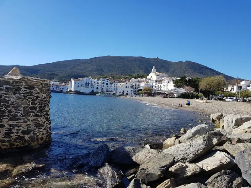 Vue d'une plage rocheuse avec un village en arrière-plan et des montagnes.