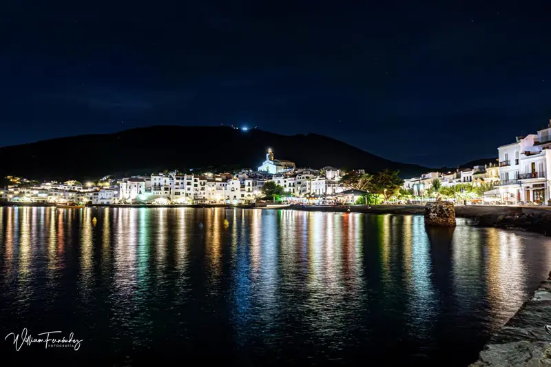 Vue nocturne d'un village côtier illuminé au bord de l'eau.