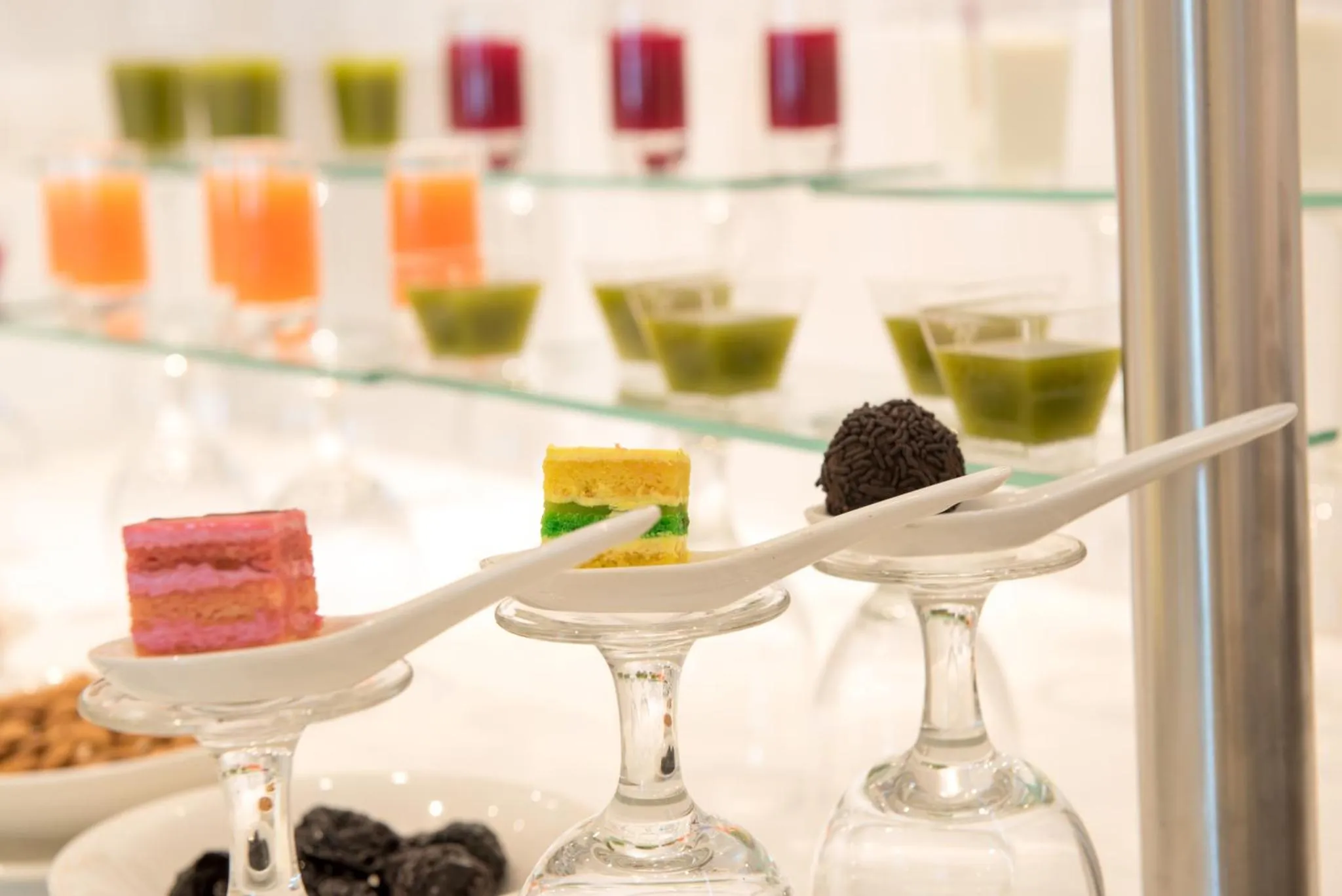 Assortiment de petites douceurs colorées présentées sur des cuillères et des verres.