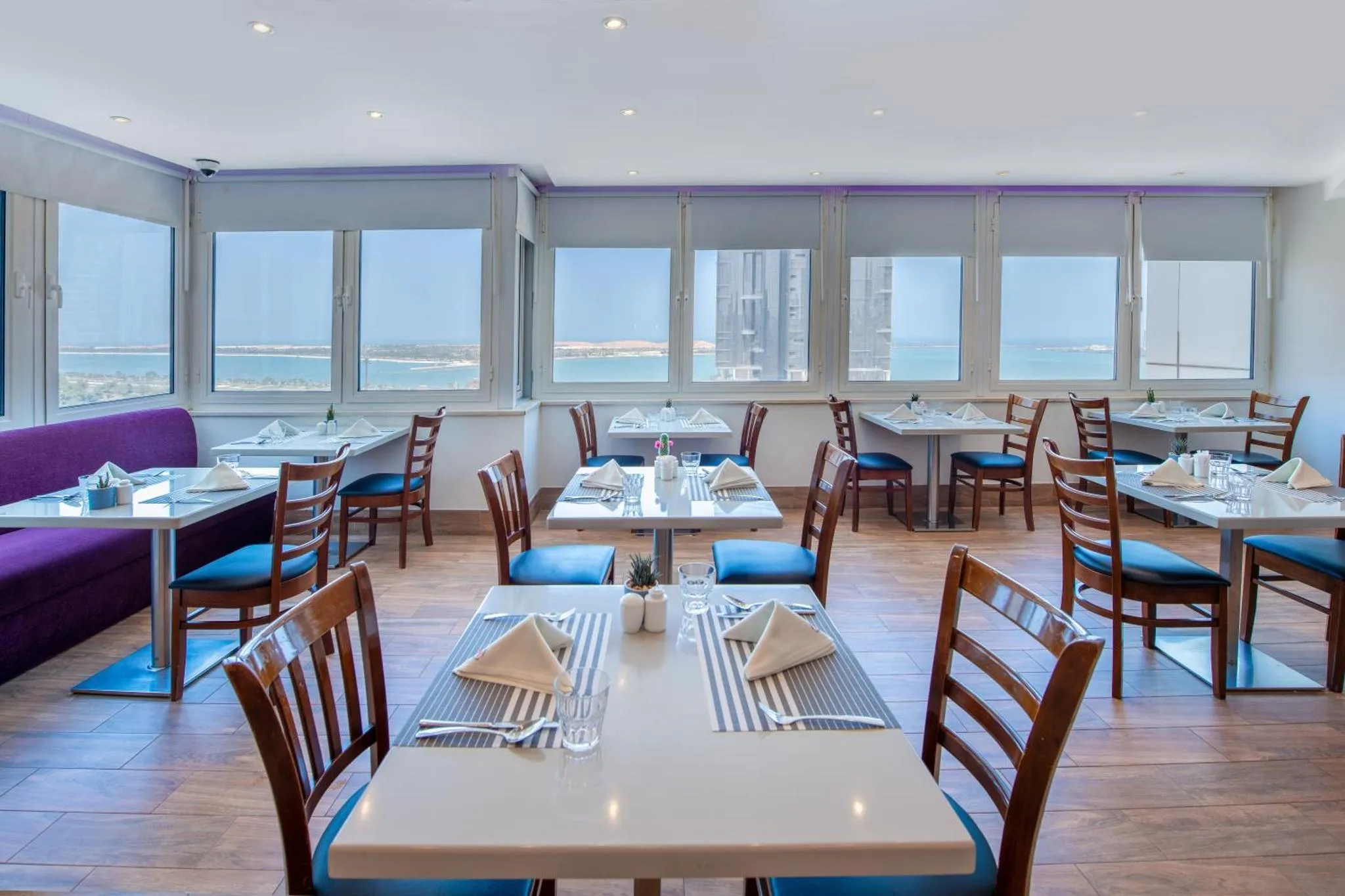 Une salle lumineuse avec des tables dressées pour le repas, face à une vue sur la mer.