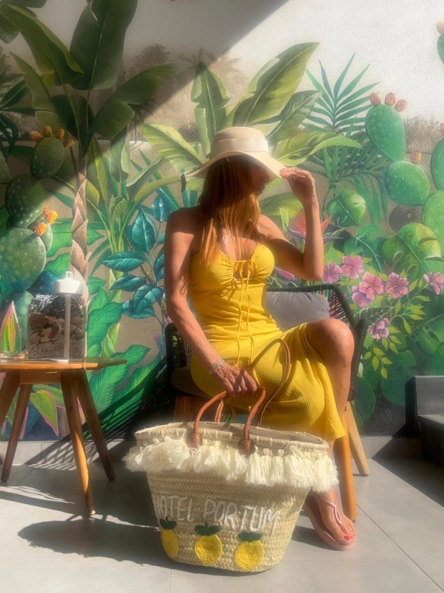 Une femme assise sur un banc devant un mur décoré de plantes tropicales.