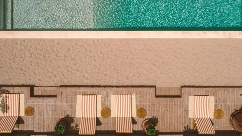 Transats rayés alignés au bord d'une piscine rectangulaire.