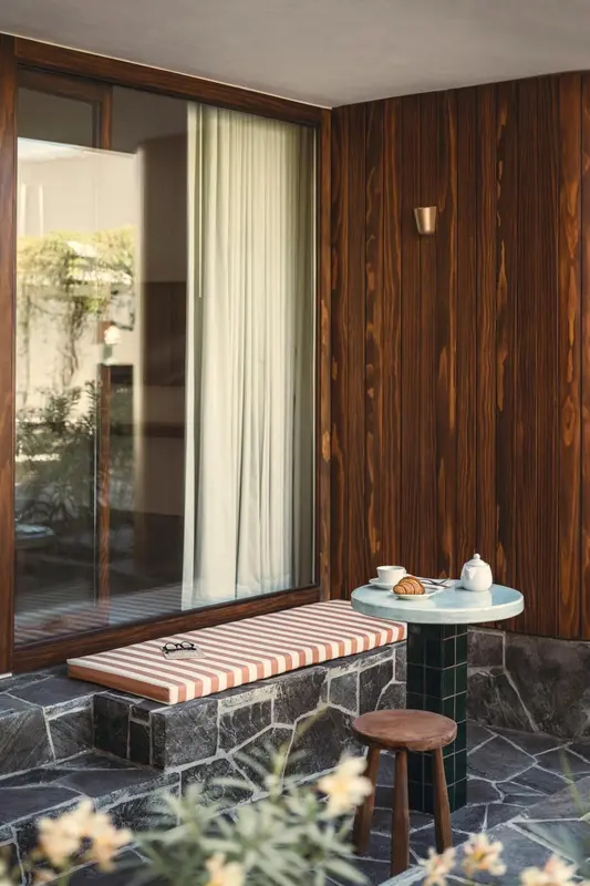Une petite table ronde et un coussin rayé se trouvent devant une fenêtre et un mur en bois.