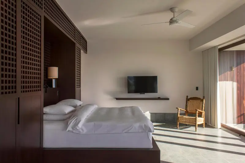 Une chambre lumineuse avec un grand lit et un fauteuil en osier.