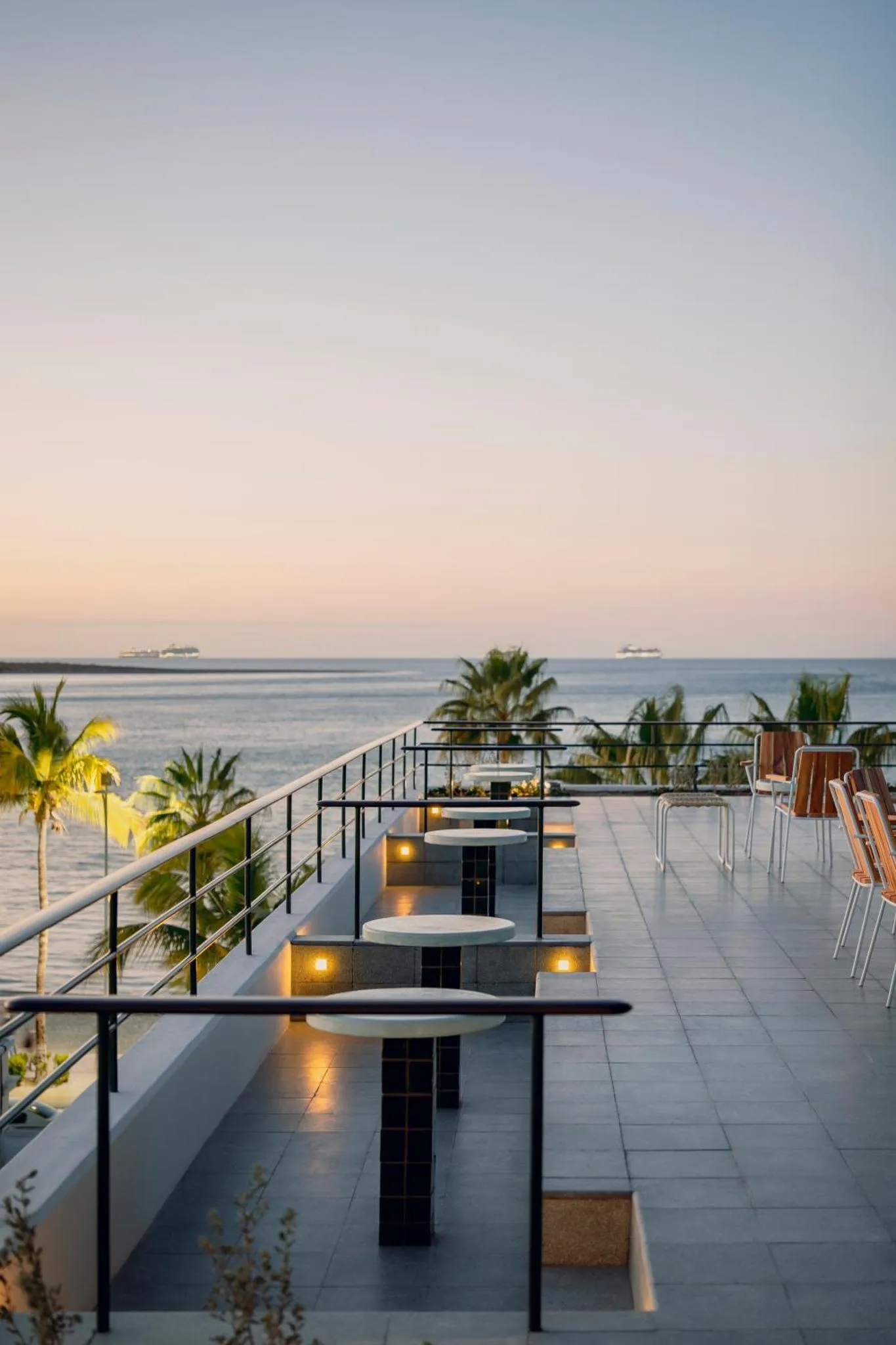 Terrasse avec tables et chaises donnant sur la mer au coucher du soleil.