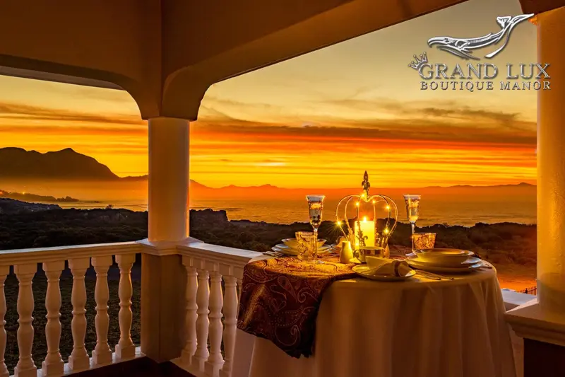 Une table dressée sur une terrasse offre une vue sur un coucher de soleil orangé au-dessus de la mer.