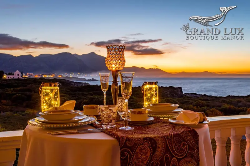 Table dressée avec des verres et de la vaisselle sur une terrasse avec vue sur la mer au coucher du soleil.