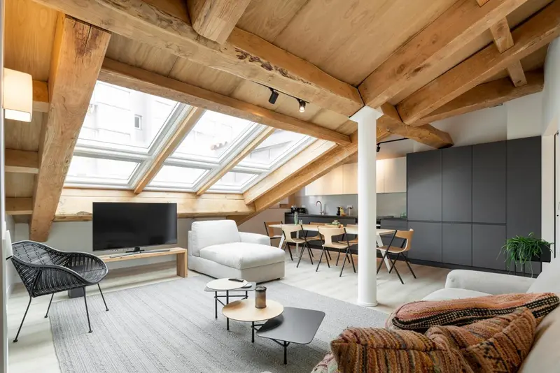 Espace de vie lumineux sous combles avec canapé et table à manger.
