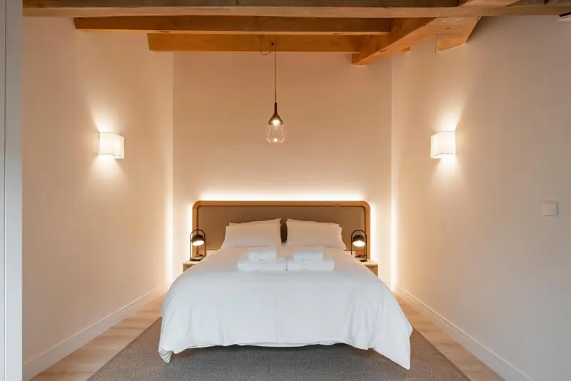 Une chambre lumineuse avec un grand lit blanc et des appliques murales.