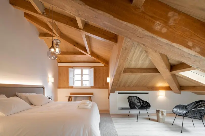 Une chambre mansardée lumineuse avec un lit et des fauteuils.
