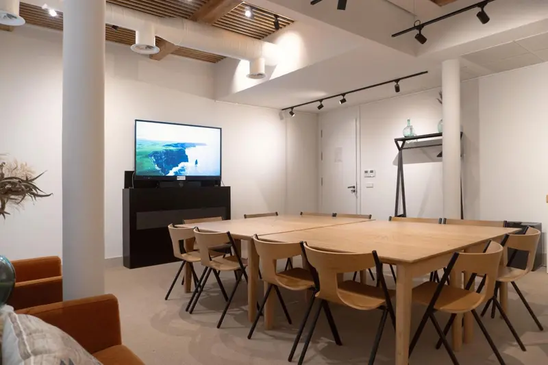 Une grande table de réunion en bois est entourée de chaises dans une pièce lumineuse.