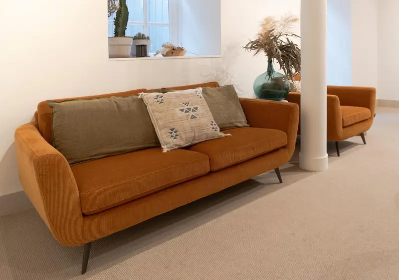 Un canapé orange et deux fauteuils dans un espace de détente.