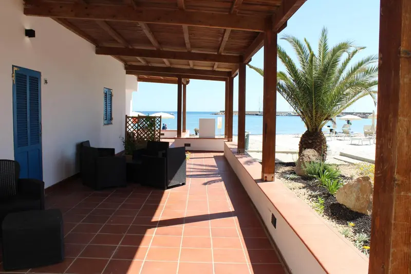 Terrasse ombragée avec mobilier de jardin donnant sur une plage ensoleillée.