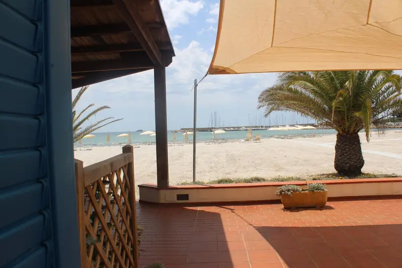 Terrasse ombragée donnant sur une plage de sable fin et la mer.