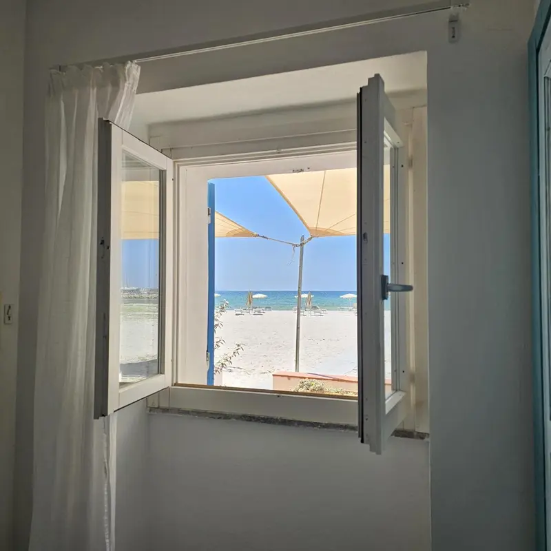 Vue sur une plage ensoleillée depuis une fenêtre ouverte.