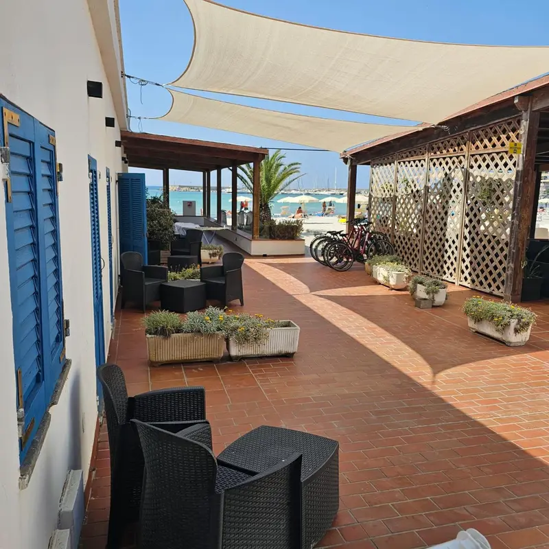 Terrasse ombragée avec mobilier de jardin et vue sur la mer.