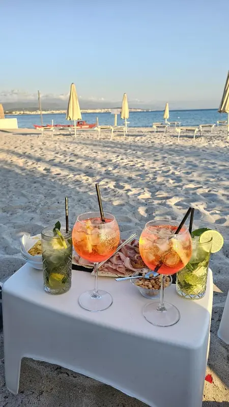 Deux cocktails colorés et des amuse-gueules sont servis sur une table basse sur une plage de sable.