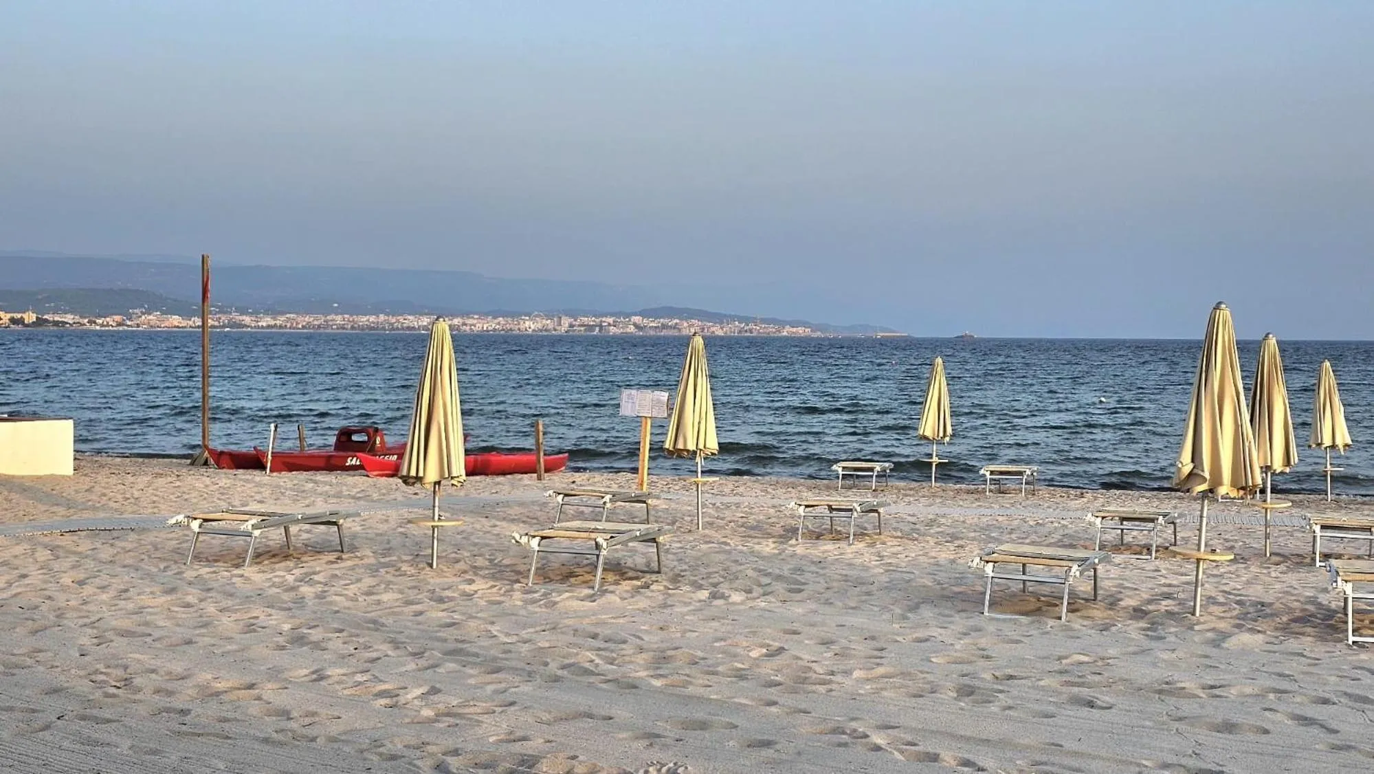 Plage de sable avec transats et parasols face à la mer.