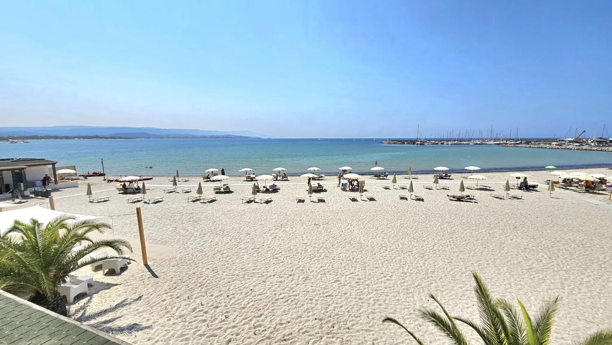 Plage de sable fin avec parasols et transats face à la mer.
