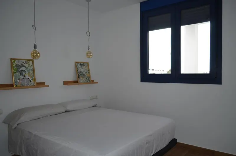 Une chambre lumineuse avec un lit simple et des suspensions décoratives.